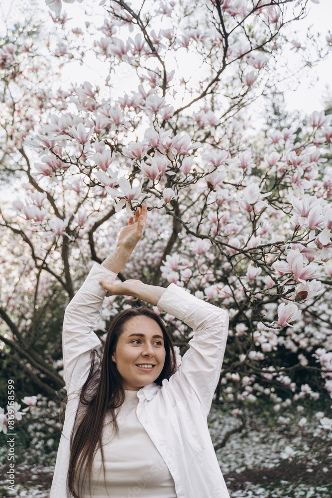 Happy young woman standing with arms raised in front of magnolia tree Happy young woman standing with arms raised in front of magnolia tree