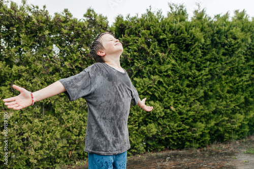 Happy boy with arms outstretched enjoying rain at garden photo