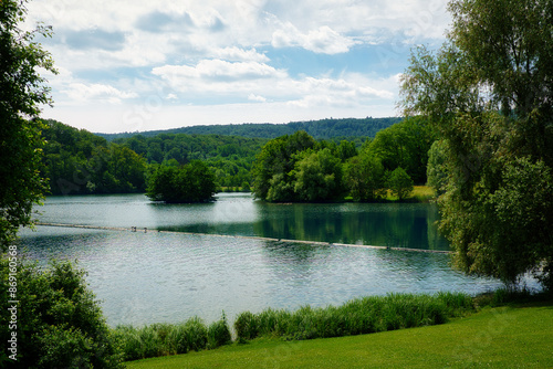 Blick auf einen idyllischen Badesee inmitten der Natur, umgeben von Wiese und Wäldern photo