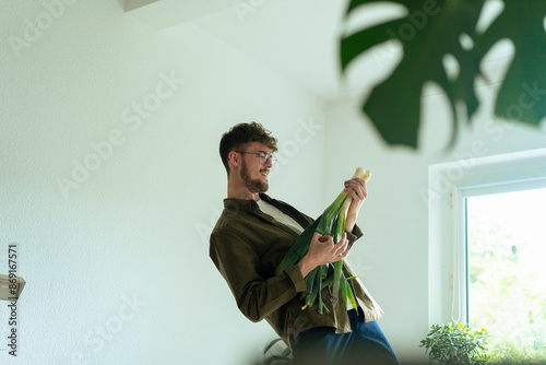 Playful young man playing air guitar with leek vegetable at home