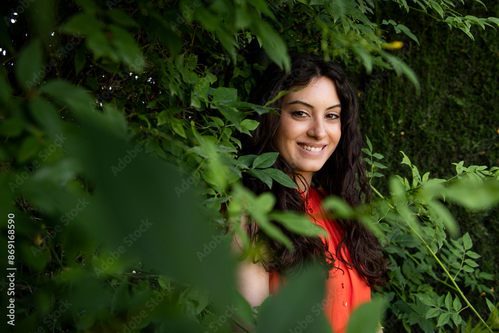 Smiling beautiful woman standing between leaves at garden