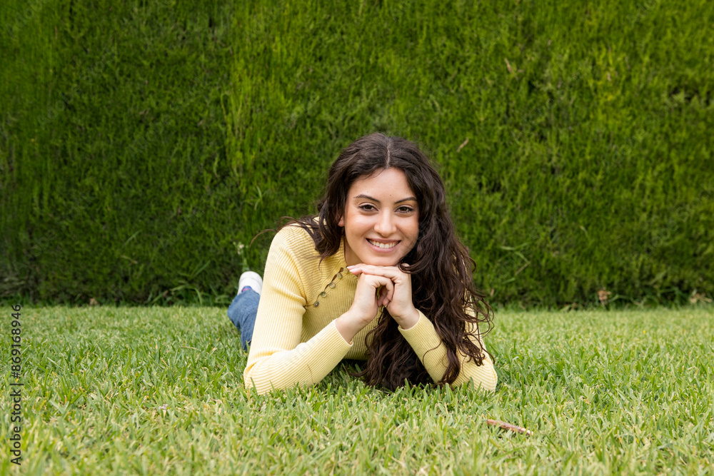 Beautiful woman with hands on chin lying on grass at garden Beautiful woman with hands on chin lying on grass at garden