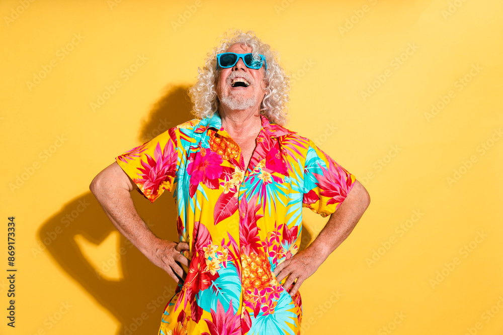 Cheerful senior man wearing sunglasses and standing with hands on hips against yellow background Cheerful senior man wearing sunglasses and standing with hands on hips against yellow background