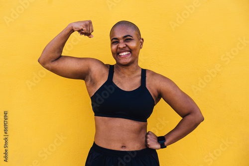 Happy muscular woman flexing muscle in front of yellow wall photo
