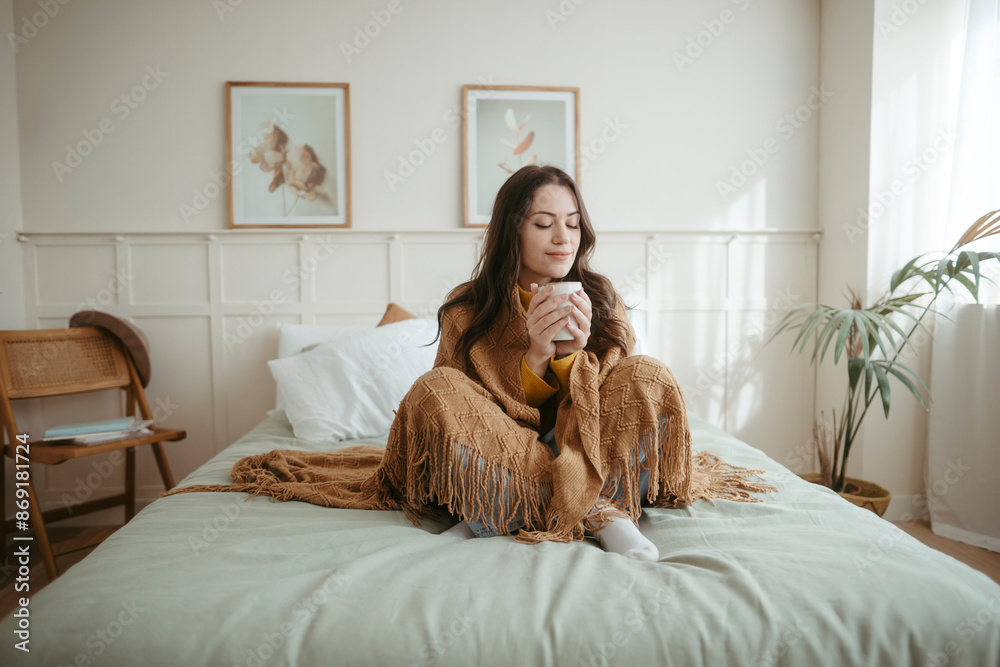 Woman covered in blanket drinking tea on bed at home Woman covered in blanket drinking tea on bed at home