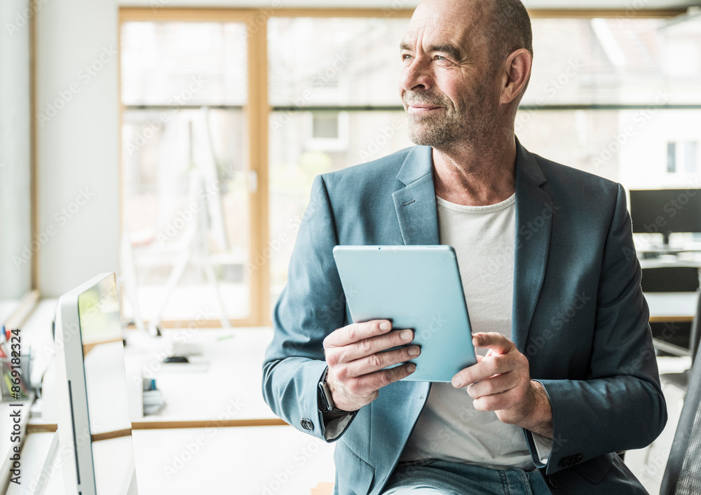 Thoughtful mature businessman looking away sitting with tablet PC at office Thoughtful mature businessman looking away sitting with tablet PC at office