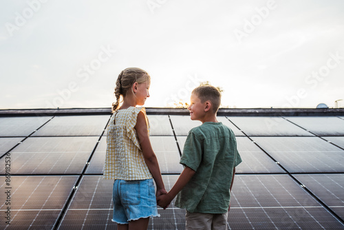 Two young siblings on roof with solar panels, looking at each other. Rooftop solar or photovoltaic system. Sustainable future for next generation. photo