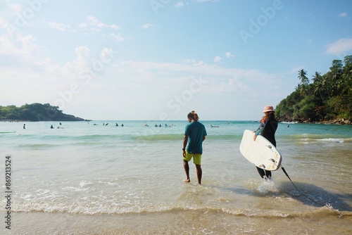 A Sri Lankan surfing coach and his student are going on the beach to the ocean to surf photo