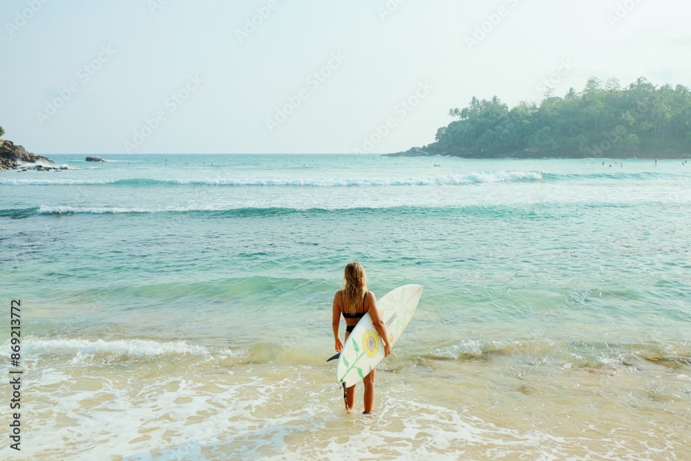 A surfer woman stands in the water by the beautiful ocean lagoon with the surfboard on the tropical beach. A surfer woman stands in the water by the beautiful ocean lagoon with the surfboard on the tropical beach.