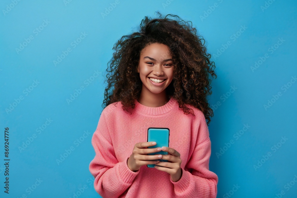 Photo of cheerful generation z american girl holding smartphone in hands smiling isolated on blue color background Photo of cheerful generation z american girl holding smartphone in hands smiling isolated on blue color background