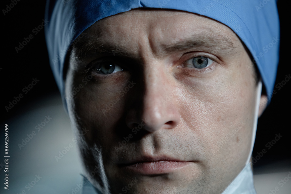 Extreme closeup portrait of young male surgeon looking at camera with dramatic light in hospital Extreme closeup portrait of young male surgeon looking at camera with dramatic light in hospital