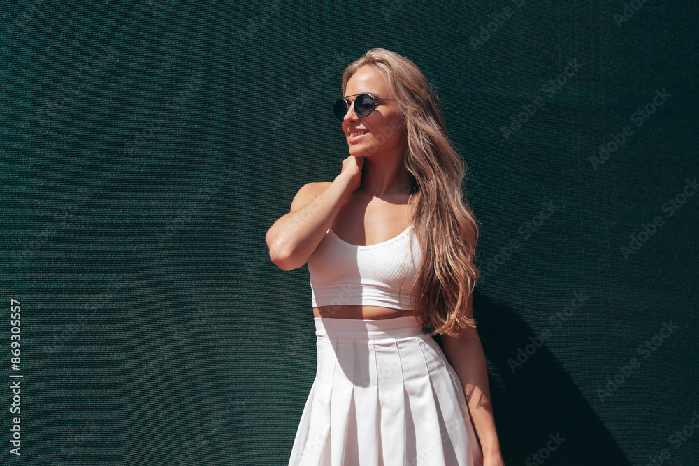 Young beautiful smiling woman wearing fashionable white dress skirt and tank top. Hot model posing on tennis court at summer sunny day. Sexy female, cheerful and happy, sunglasses Young beautiful smiling woman wearing fashionable white dress skirt and tank top. Hot model posing on tennis court at summer sunny day. Sexy female, cheerful and happy, sunglasses