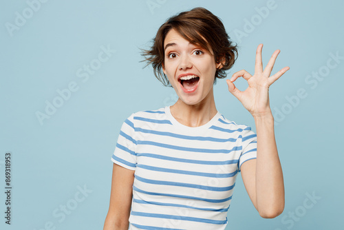 Young happy surprised shocked woman she wears striped t-shirt casual clothes showing okay ok gesture look camera isolated on plain pastel light blue cyan background studio portrait. Lifestyle concept. photo