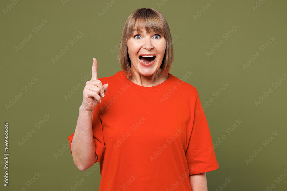 Elderly smart blonde woman 50s year old she wear orange t-shirt casual clothes holding index finger up with great new idea isolated on plain pastel green background studio portrait. Lifestyle concept Elderly smart blonde woman 50s year old she wear orange t-shirt casual clothes holding index finger up with great new idea isolated on plain pastel green background studio portrait. Lifestyle concept