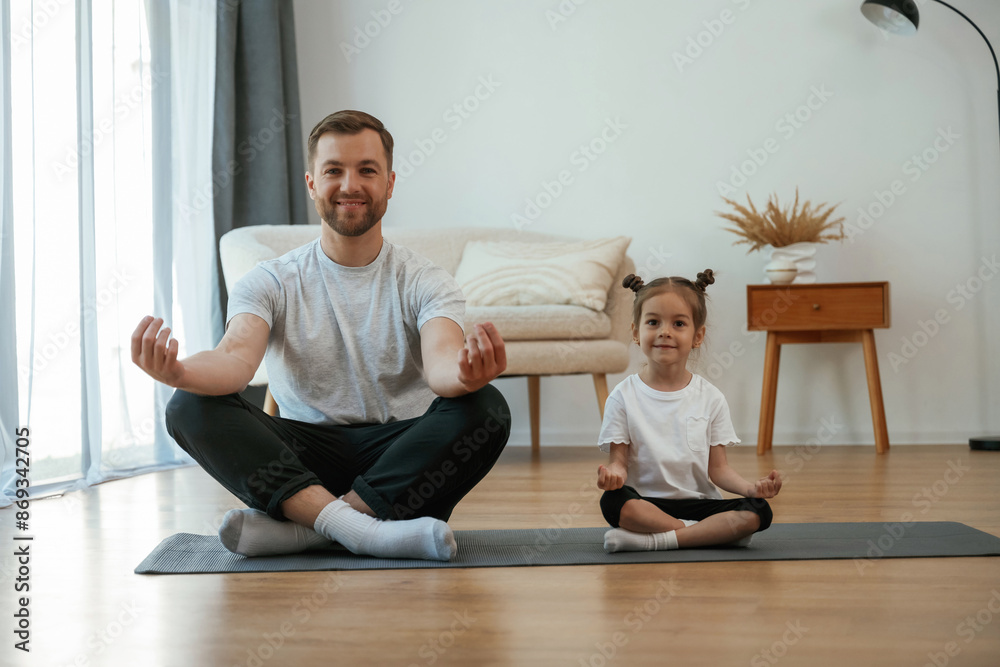 © standret - Lotus pose. Father with little daughter are doing yoga at home
