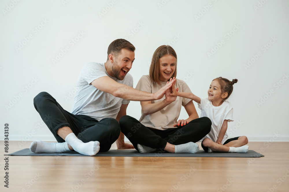 Doing high five. Family of mother, father and daughter are doing yoga at home Doing high five. Family of mother, father and daughter are doing yoga at home