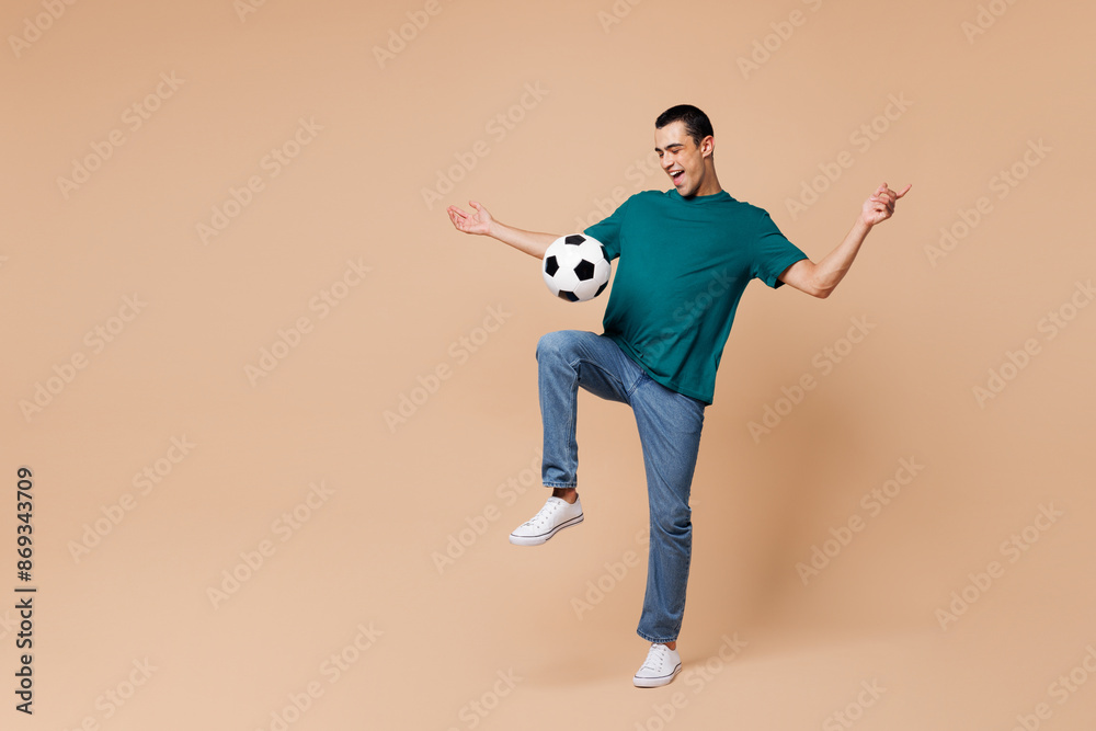 Full body young happy excited fun man fan wear basic blue t-shirt cheer up support football sport team hold soccer ball dribbling watch tv live stream isolated on plain pastel beige background studio Full body young happy excited fun man fan wear basic blue t-shirt cheer up support football sport team hold soccer ball dribbling watch tv live stream isolated on plain pastel beige background studio