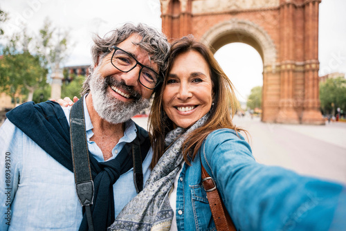 Married couple taking selfie in front of Triumphal Arch in Barcelona, Catalonia, Spain - Husband and wife enjoying romantic moment together at summer holiday in Europe