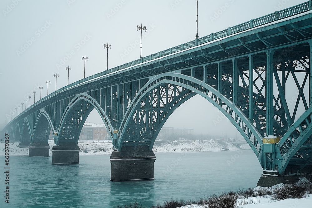 A cold, overcast winter setting revealing a snowy landscape with an imposing steel blue bridge with arch designs