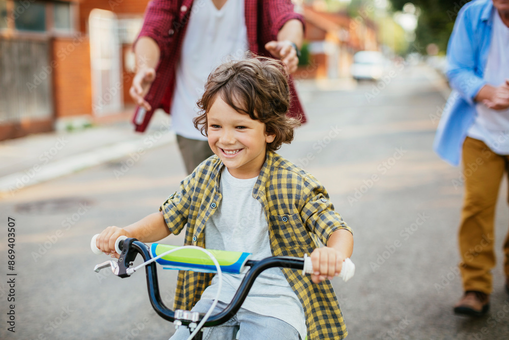 Obraz premium Father and grandfather teaching young boy to ride a bike on residential street