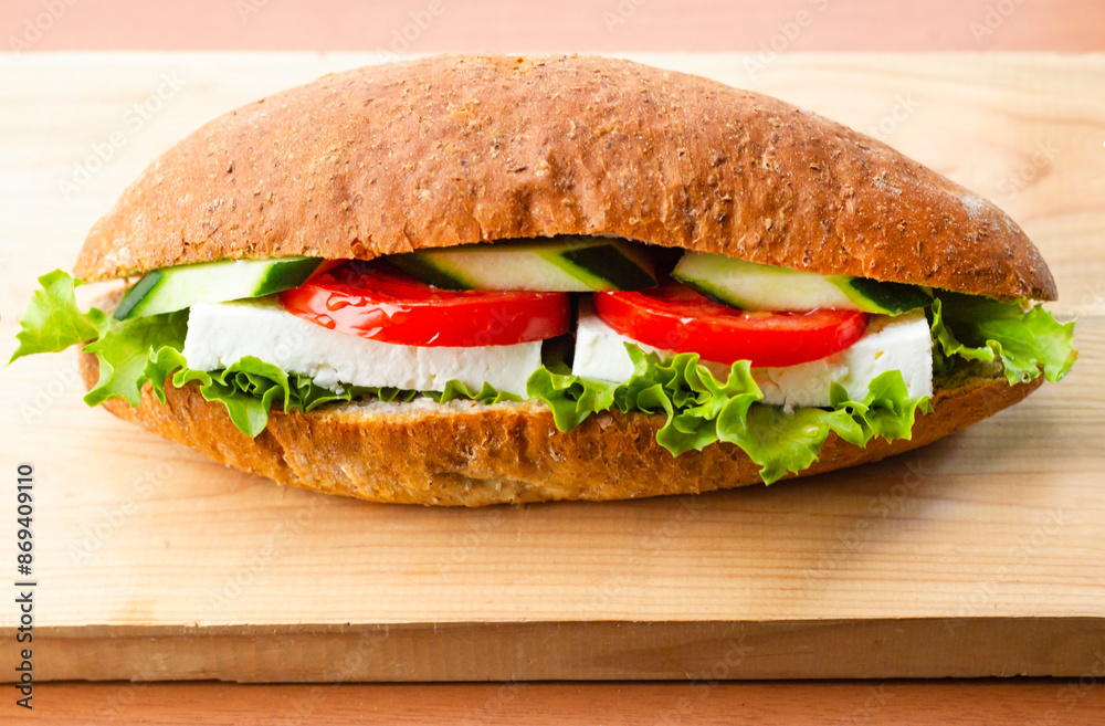 A sandwich with tomato, cucumber, feta cheese, lettuce on wooden plate A sandwich with tomato, cucumber, feta cheese, lettuce on wooden plate