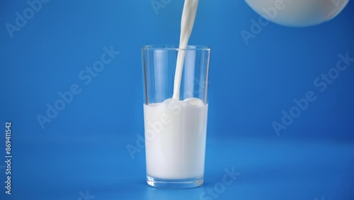 Pouring delicious organic fresh milk into glass in light blue background, natural food from eco farm