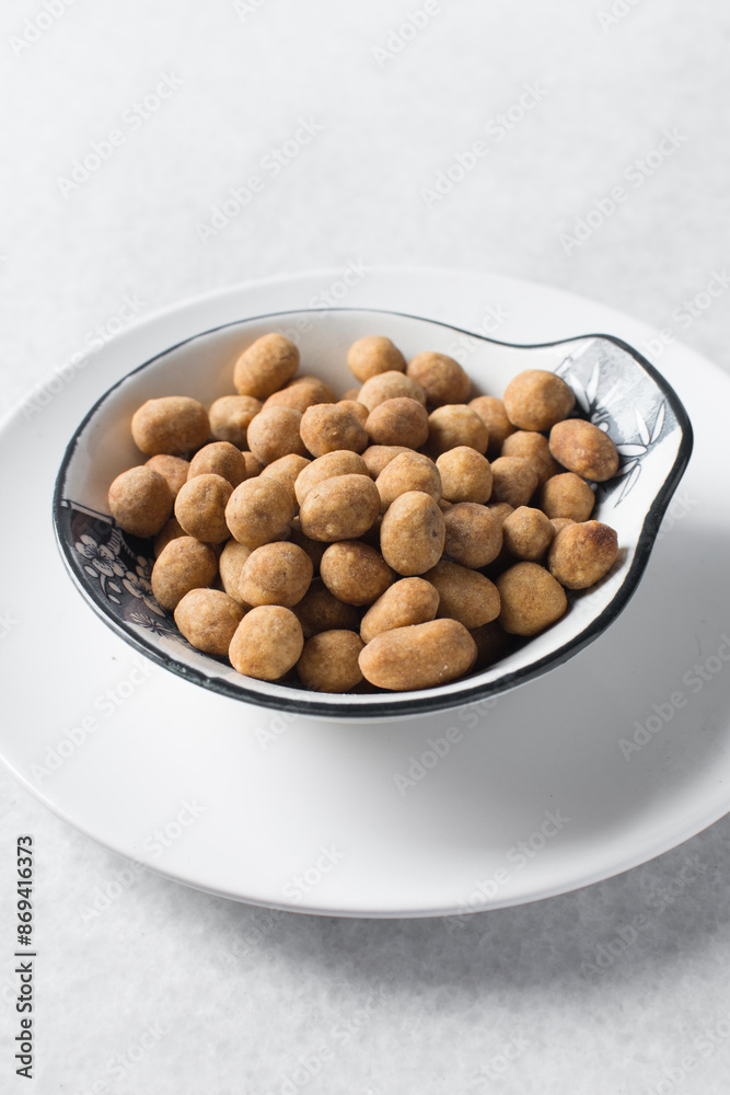 Fried coated peanuts in a white ceramic plate, cracker peanuts on a marble countertop, nigerian peanut snack in a small white plate