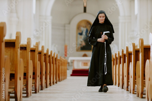 Fototapete Wide shot of senior Caucasian nun holding Bible book walking along nave in Catho