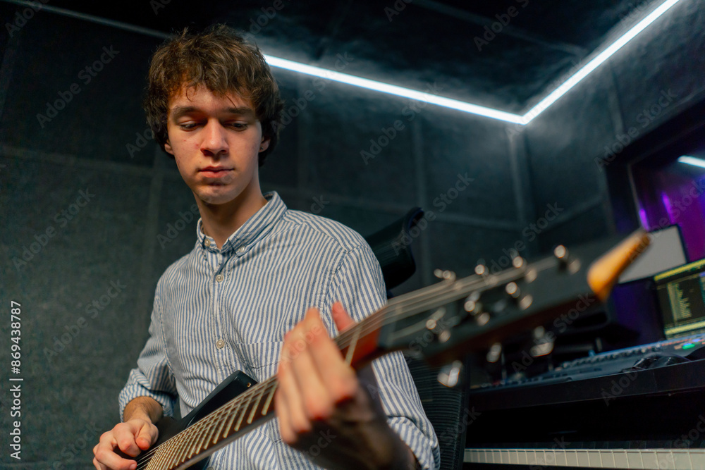 Obraz premium in the recording room equipment the sound of music a handsome young guy plays an electric guitar plucks the strings choosing the right note