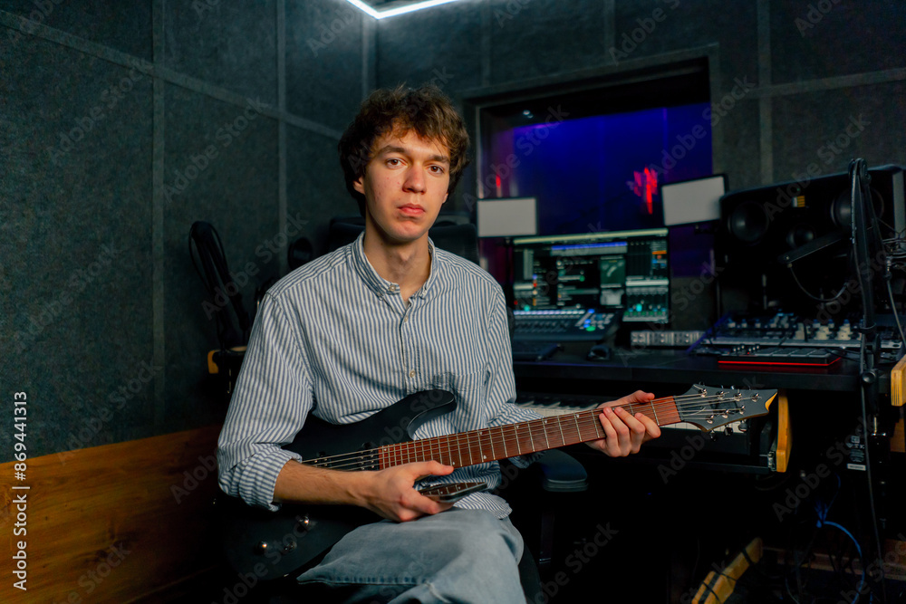 Obraz premium in the recording room equipment the sound of music handsome young guy tunes a guitar plucks the strings selecting the desired sound tonality