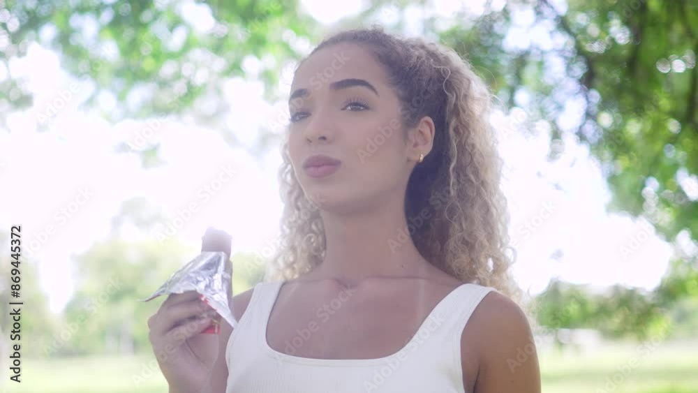 Athletic young woman enjoying a refreshing snack outdoors. Active female pausing for a quick energy boost in a lush park setting Athletic young woman enjoying a refreshing snack outdoors. Active female pausing for a quick energy boost in a lush park setting