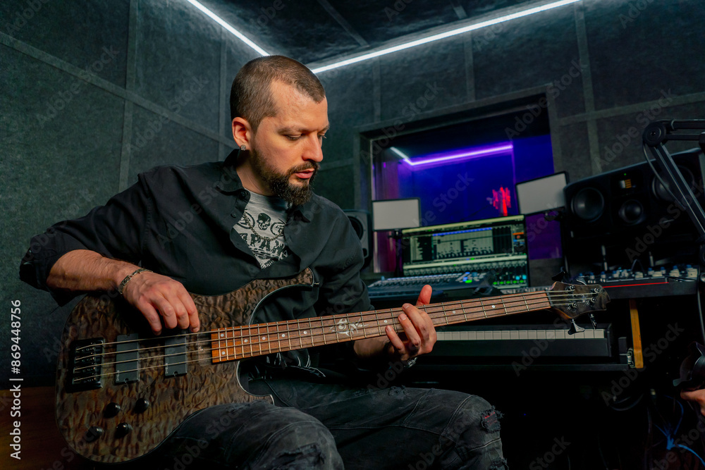 Obraz premium in the equipment of a recording room handsome man with a beard and tattoos plays an electric guitar plucks the strings choosing the right note