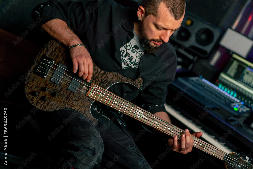 Obraz premium in the equipment of a recording room handsome man with a beard and tattoos plays an electric guitar plucks the strings choosing the right note