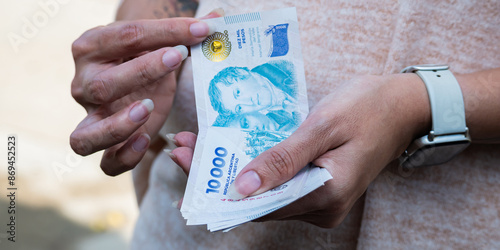 Tableau sur toile Woman counting 10,000 Argentine peso bills.