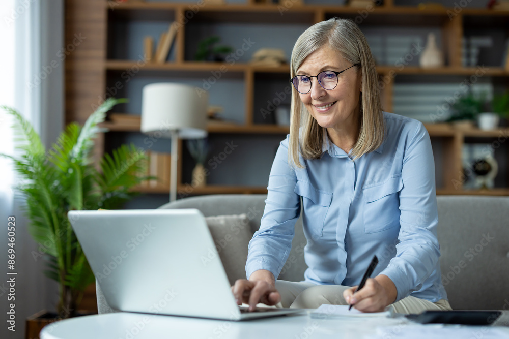 Smiling senior woman working on a laptop at her home office. She's taking notes and appears focused and happy. Perfect for concepts of remote work, home office, senior professionals, and technology Smiling senior woman working on a laptop at her home office. She's taking notes and appears focused and happy. Perfect for concepts of remote work, home office, senior professionals, and technology