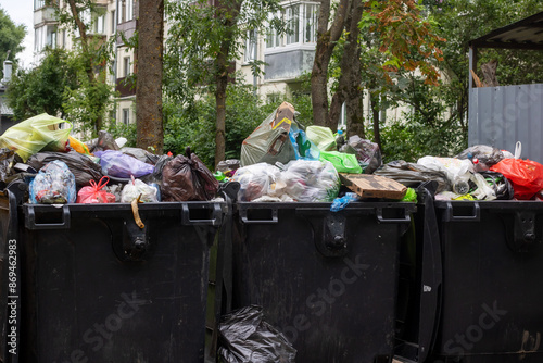 Canvas Print A row of garbage cans filled with trash on a city street with a tree nearby