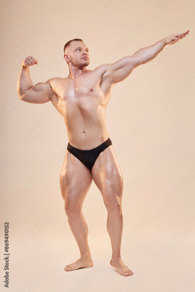 Fototapeta premium Full shot of topless strong bodybuilder in archer pose. Powerful sportsman posing with arm clenching fist on neutral background, copy space