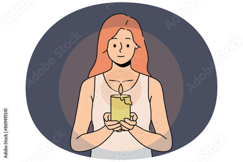 Woman with candle in hands looks at fire, performing religious ritual or seance. Positive girl holding candle to light way in dark due to power outage in house or broken lighting fixtures
