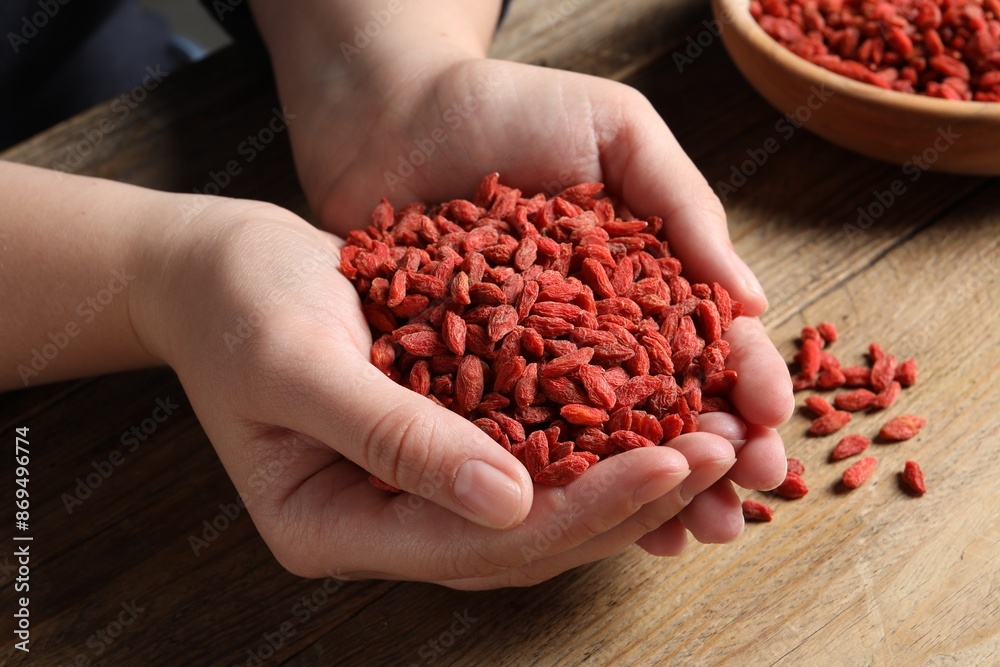 Woman holding pile of dried goji berries at wooden table, closeup Woman holding pile of dried goji berries at wooden table, closeup