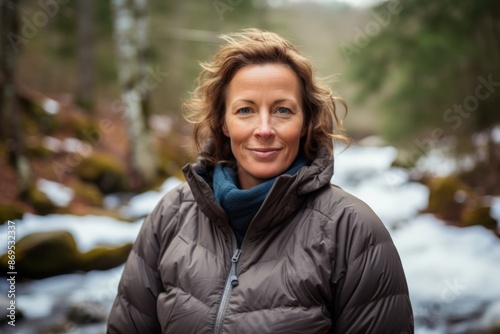 Portrait of a cheerful woman in her 40s sporting a quilted insulated jacket while standing against tranquil forest stream © Markus Schröder