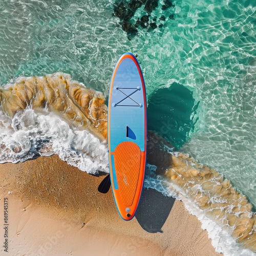 A colorful paddleboard on the beach, with an orange and blue colorway, bird's eye view photo