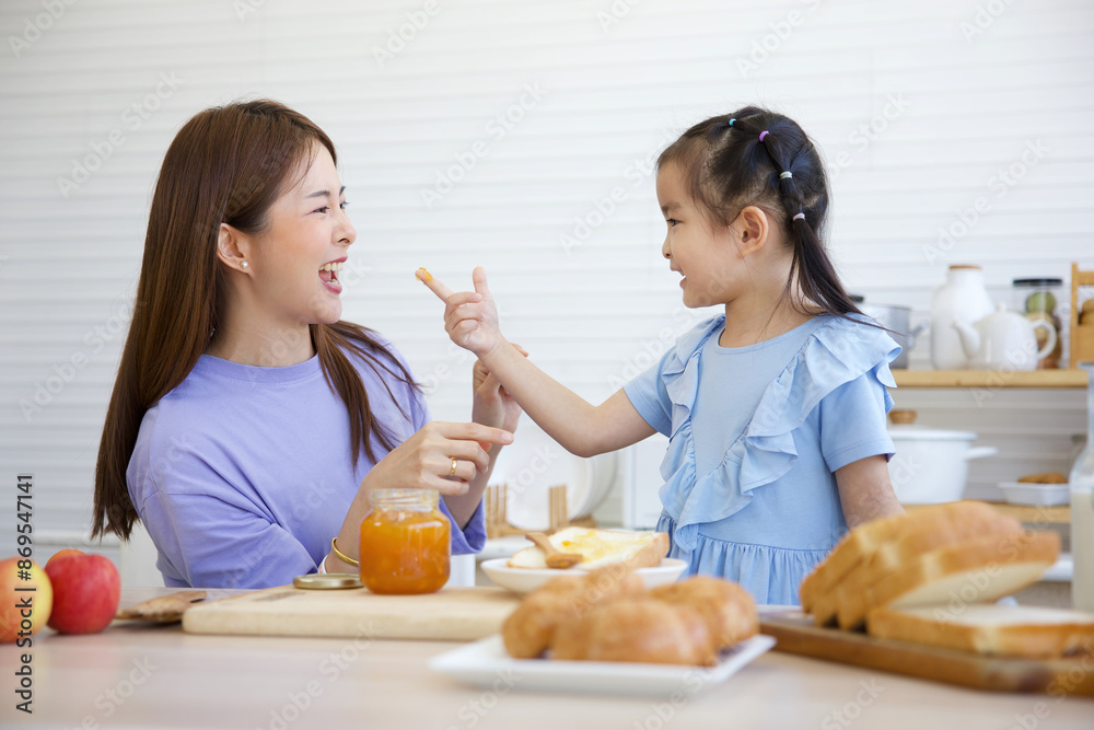 mother tasting orange jam with her daughter in the kitchen mother tasting orange jam with her daughter in the kitchen