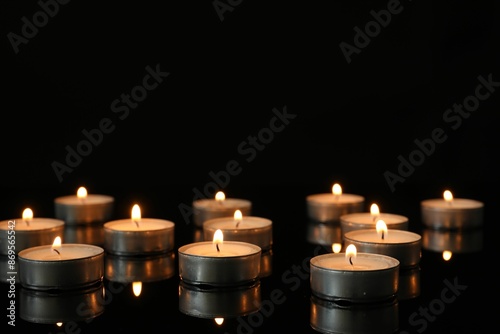 Quadro su tela Many burning tealight candles on mirror surface against black background
