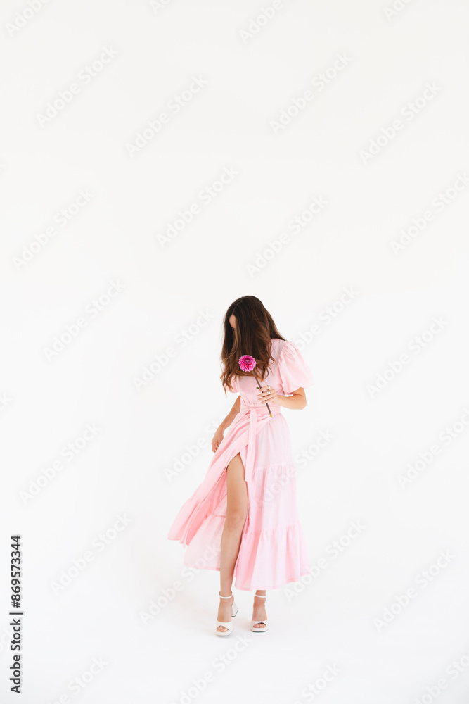 Details of everyday elegant look. Sensual model wearing evening outfit. Pink cocktail dress with puff sleeves shoulders in trendy minimalistic style. Beautiful brunette woman hold pink flower. Details of everyday elegant look. Sensual model wearing evening outfit. Pink cocktail dress with puff sleeves shoulders in trendy minimalistic style. Beautiful brunette woman hold pink flower.