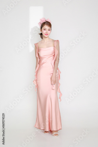 Stylish young fashionable Asian woman in a stunning pink dress, trendy makeup with light shining through a slit on her, posing on an isolated white background.
