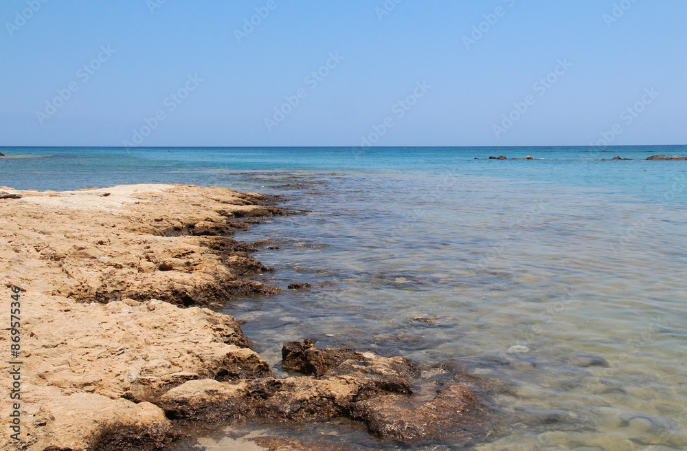 Rocky beach of the Mediterranean Sea, seaside resort of Cyprus island, Protaras. The stones are visible from the clear sea water on a sunny summer day. Natural daylight. Natural wallpaper Rocky beach of the Mediterranean Sea, seaside resort of Cyprus island, Protaras. The stones are visible from the clear sea water on a sunny summer day. Natural daylight. Natural wallpaper