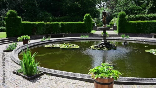 Green park, garden and pond in front of a brick flooring and glass under a warm and sunny summer weather