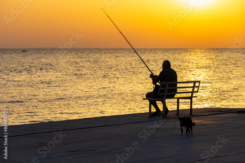 Silhouettes of a fisherman and a cat at sunset at Nikiti Marina, Sithonia, Chalkidiki peninsula, Central Macedonia, Northern Greece, Aegean Sea coast