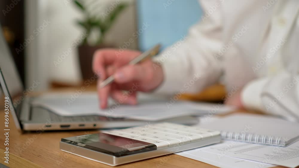 Man Sitting at Desk in Office Diligently writing on Piece of Paper, Calculates Costs and Revenues on Calculator, close up. Unrecognizable person freelancer. Male Businessman working at home office Man Sitting at Desk in Office Diligently writing on Piece of Paper, Calculates Costs and Revenues on Calculator, close up. Unrecognizable person freelancer. Male Businessman working at home office