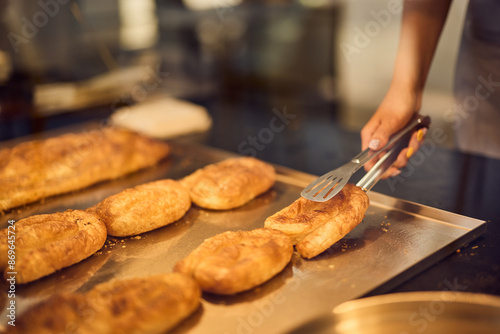 A female baker is catching a fresh pastry from a glass case.